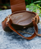 A brown and olive green leather shoulder bag with gold-tone chain details, shown open with its strap draped across a gray stone surface outdoors.