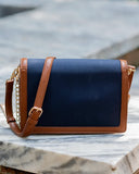 A navy blue canvas shoulder bag with tan leather trim and a gold chain strap, resting on a white marble surface.