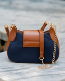 A navy blue and brown handbag with gold chain details, resting on a gray stone surface.