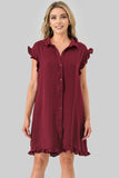 A woman modeling a short-sleeve button-front dress in deep burgundy with ruffled trim at the collar, sleeves, and hem, against a plain light gray studio background.
