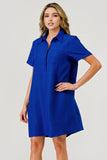 A woman modeling a short-sleeve collared shift dress in a vibrant royal blue color, featuring a subtle textured crinkle pattern, set against a plain light gray studio background.