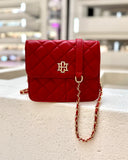 Red quilted handbag with gold chain on a textured surface