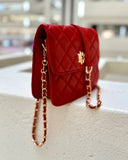 Red quilted handbag with gold chain strap on a light surface