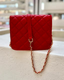 Red quilted handbag with a gold chain strap on a light surface.