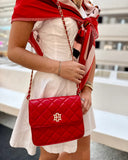 Person holding a red quilted handbag with a brand logo, wearing a white dress and red shawl.