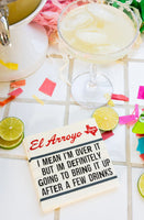 Glass of margarita with lime wedges, colorful straws, and a sign reading 'El Arroyo' on a checkered tablecloth.