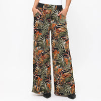 Tropical leaf patterned pants worn by a person on a white background