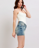 Woman wearing a white tank top and denim shorts on a plain background