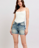Woman wearing a white top and denim shorts on a plain background