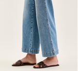 Cropped image of a person wearing blue jeans and brown sandals on a light background