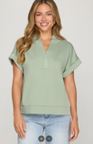 Woman wearing a light green short-sleeve top with a zipper on a plain background