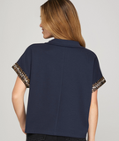 Navy blue shirt with leopard print sleeves worn by a person on a gray background