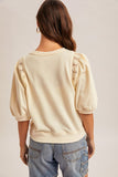 Woman wearing a beige top with lace sleeves on a plain background
