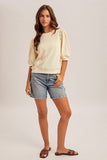 Woman wearing a beige top and denim shorts on a plain background