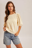 Woman wearing a beige top with lace sleeves and denim shorts on a plain background