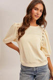 Woman wearing a beige blouse with lace details on a plain background