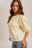 Woman wearing a beige sweater with lace sleeves on a plain background