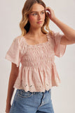 Woman wearing a pink smocked top and blue jeans against a plain background