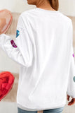 White long-sleeve top with colorful designs on sleeves, held by a person.
