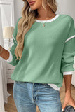 Person wearing a green ribbed sweater with white trim and blue jeans indoors.
