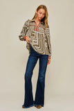 A woman modeling a long-sleeve collared blouse with a brown, beige, and white geometric pattern and red trim, paired with dark blue flare jeans, against a solid light beige studio background.