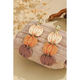 Pumpkin-shaped earrings on a wooden surface with a natural background