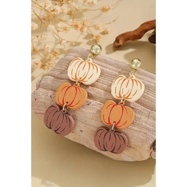 Pumpkin-shaped earrings on a wooden surface with a natural background