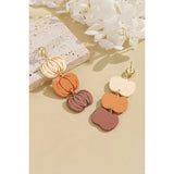 Colorful pumpkin-shaped earrings on a beige surface with white flowers in the background
