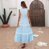 Woman in a light blue dress standing in front of a white wall with a wooden door and cactus plant.