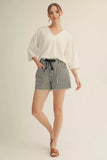 Woman wearing a white blouse and striped shorts on a beige background