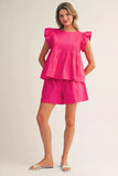 Woman wearing a bright pink outfit with ruffled sleeves on a plain background