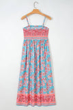 A sleeveless maxi dress with thin straps, featuring a turquoise blue and pink floral pattern, hanging on a wooden hanger against a plain white wall.