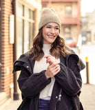 Woman wearing a coat, beanie, and sweater on a city street.