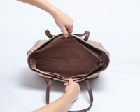 Brown leather bag with a hand opening it on a white background