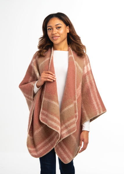 Woman wearing a pink plaid poncho over a white shirt and jeans on a white background