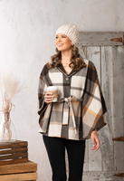 Woman wearing a plaid poncho and holding a coffee cup indoors.