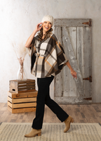 Woman wearing a plaid poncho and black pants in a rustic setting with wooden crates and a wooden door.