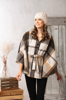 Woman wearing a plaid poncho and knit hat indoors with a wooden background