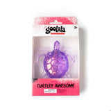 A purple glittery turtle-shaped product in retail packaging, with the brand name 'goolala' visible at the top and the text 'TURTLEY AWESOME' on the lower pink section of the box.