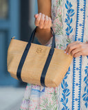 Person holding a straw handbag with black straps, wearing a floral dress.