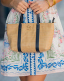 Person holding a straw handbag with a floral dress in the background