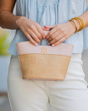 Person holding a beige and pink handbag with a logo, wearing a light blue top and white pants.