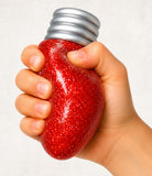 Hand holding a red glittery light bulb with a silver base against a white background